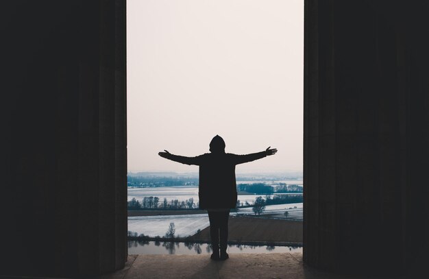 Silhouet man met uitgestrekte armen die op de muur staat tegen een heldere lucht