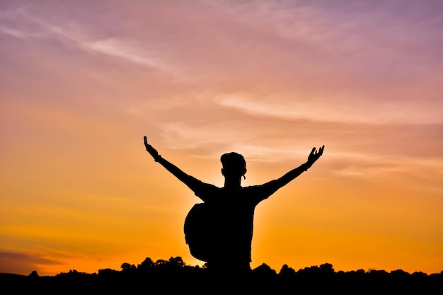 Silhouet man met uitgestrekte armen tegen bewolkte lucht tijdens zonsondergang