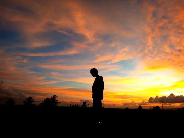 Silhouet man staan op het veld tegen de hemel tijdens zonsondergang.