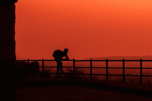 Foto silhouet man staande bij de reling tegen de heuvel tijdens de zonsondergang