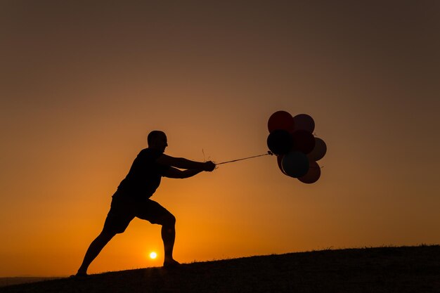 Foto silhouet man trekt ballonnen tegen een heldere lucht tijdens zonsondergang