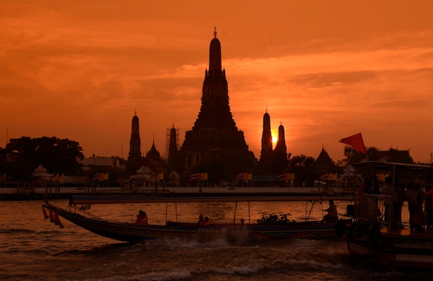 Silhouet man zeilboot in de rivier met tempel op de achtergrond tegen oranje hemel