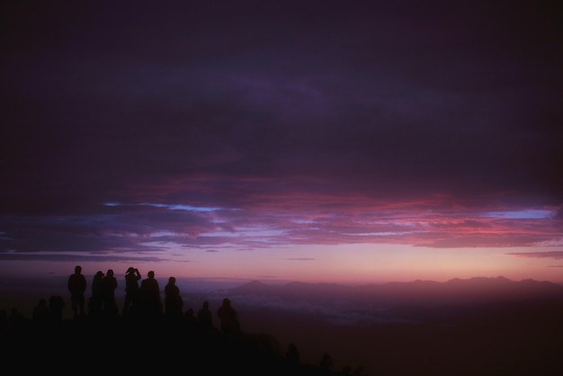 Silhouet mensen staan op de berg tegen bewolkte lucht tijdens de zonsondergang