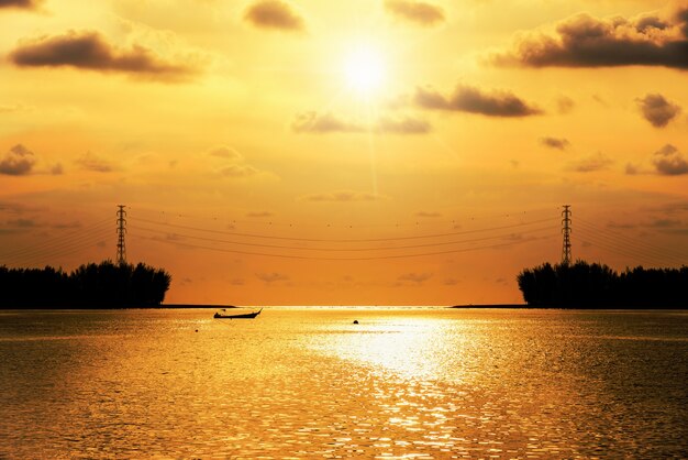 Silhouet mooi landschap hoogspanning elektriciteitsmast kabelverbinding over de baai bij zonsondergang over de zee, zon en wolk aan de hemel met een fel oranje en geel, Thailand