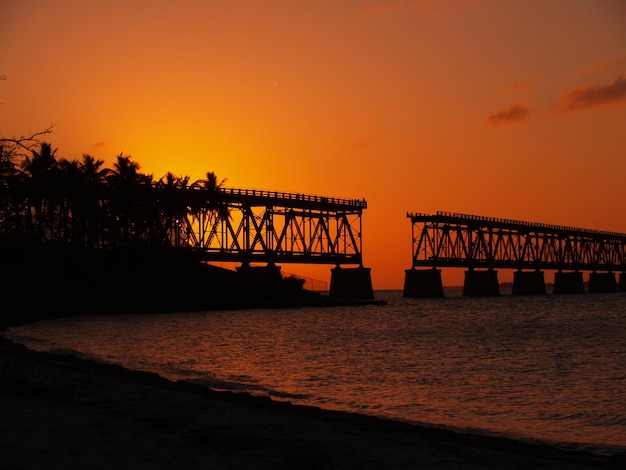 Foto silhouet onvolledige brug op het meer tegen oranje lucht