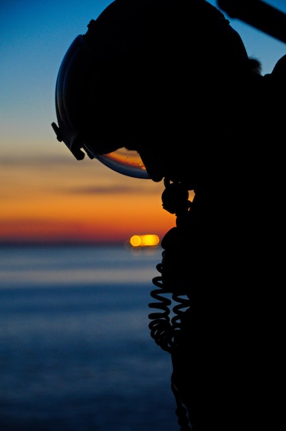 Silhouet piloot in helikopter tegen de zee tijdens zonsondergang
