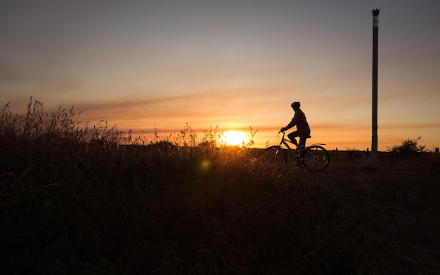 Silhouet tienermeisje fietsen op het land tegen de hemel tijdens zonsondergang