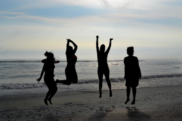 Silhouet van 4 vrouwen die bij zonsondergang op een strand springen