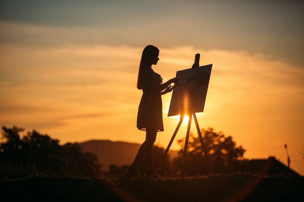 Silhouet van blond meisje schildert een schilderij op het doek. Palet met verf en spatel, zonnige zomerdag