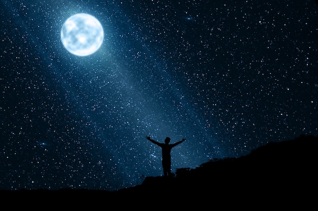 Silhouet van de gelukkige mens die van de nacht met maan en sterren geniet