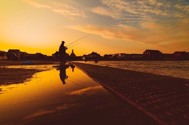 Silhouet van de visser weerspiegeld in het water bij zonsondergang