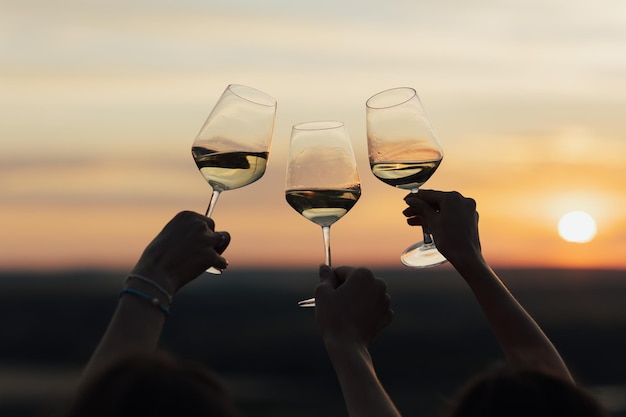 Silhouet van drie wijnglazen die roosteren met de zonsondergang op de achtergrond