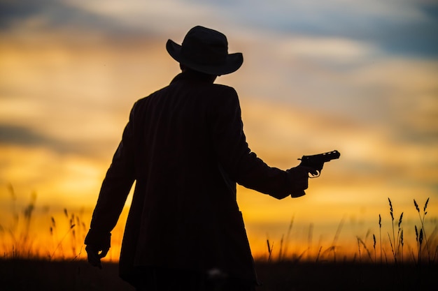 Silhouet van een cowboy in een hoed met een revolver tegen een dramatische zonsonderganghemel Westers concept Leven in het wilde westen