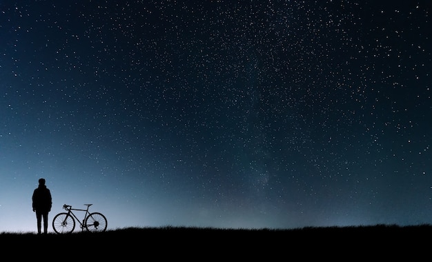 Silhouet van een fietser met een fiets die zich dichtbij de sterrenhemel bevindt.