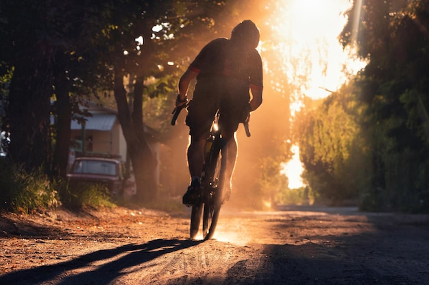 Foto silhouet van een fietser op een grindfiets in een wolk stof man rijdt op een fiets op een grindweg bij zonsondergang