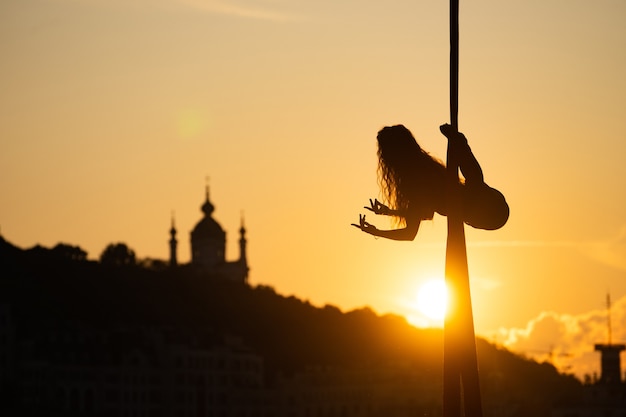 Silhouet van een flexibele vrouwenacrobaat op luchtzijde tijdens een zonsondergang op de stadsachtergrond van kiev. concept van vrijheid en vrede.