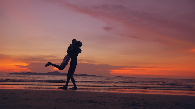 Silhouet van een gelukkig liefdevol paar ontmoeten en spelen op het strand bij zonsondergang in de oceaankust