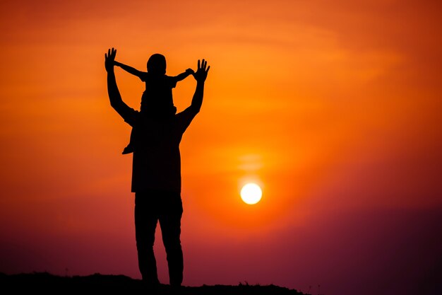 Silhouet van een gezin met een jongen die vrolijk op de nek van zijn vader rijdt tegen de avondrood