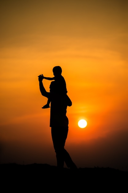 Silhouet van een gezin met een jongen die vrolijk op de nek van zijn vader rijdt tegen de avondrood