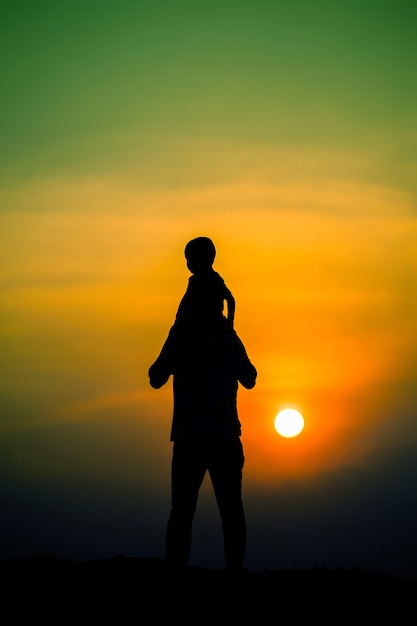 Silhouet van een gezin met een jongen die vrolijk op de nek van zijn vader rijdt tegen de avondrood