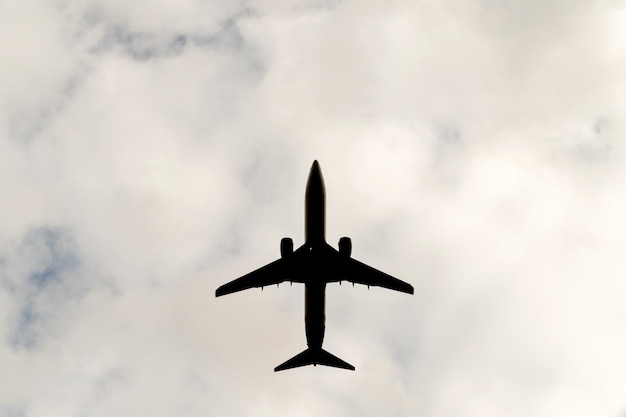 Silhouet van een groot vliegend vliegtuig tegen een achtergrond van een bewolkte hemel, een onderaanzicht