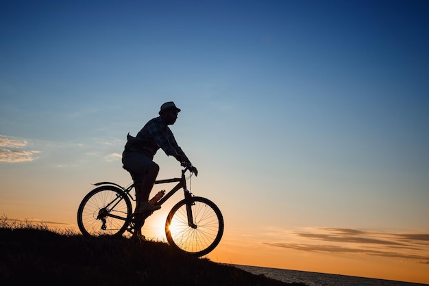 Silhouet van een hipstermens op een fiets op zonsondergangachtergrond