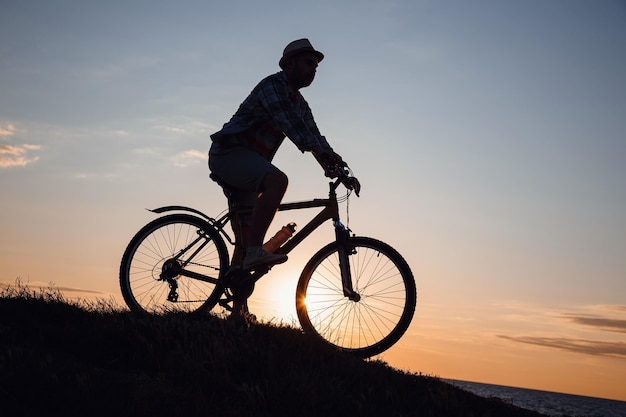 Silhouet van een hipstermens op een fiets op zonsondergangachtergrond