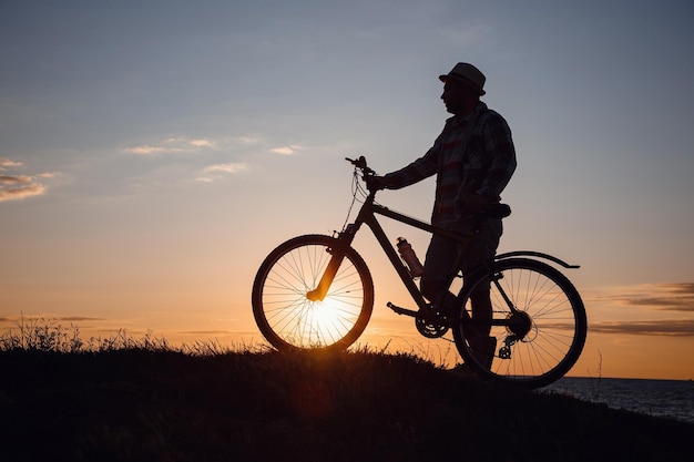 Silhouet van een hipstermens op een fiets op zonsondergangachtergrond