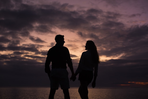 Silhouet van een jong koppel bij zonsondergang op het strand in de buurt van de oceaan