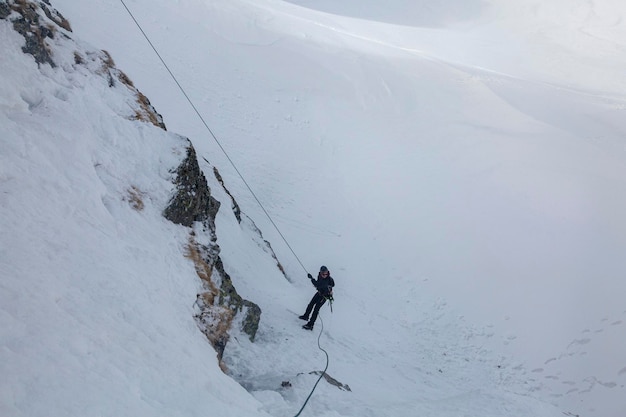 Silhouet van een jonge man die abseilt vanaf een besneeuwde klif Man op een bergbeklimmer die naar beneden afdaalt