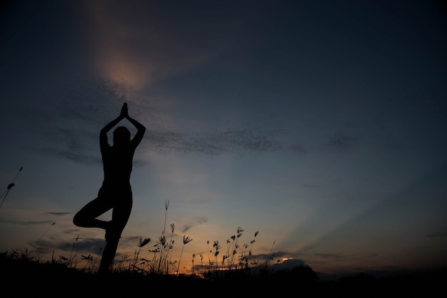 Silhouet van een jonge vrouw die yoga beoefent bij zonsondergang