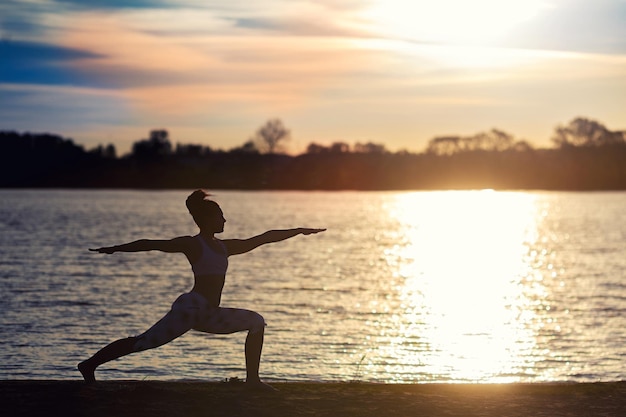 Silhouet van een jonge vrouw die yoga-oefeningen doet op het meerstrand bij zonsondergang