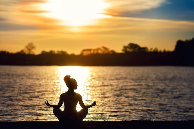 Silhouet van een jonge vrouw die yoga-oefeningen doet op het meerstrand bij zonsondergang