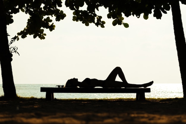 Silhouet van een jonge vrouw in bikini, liggend op het bankje in de buurt van de zee