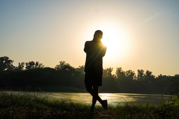 Silhouet van een jongen die oefeningen doet in het park in de buurt van zon en rivier - gezondheidsconcept