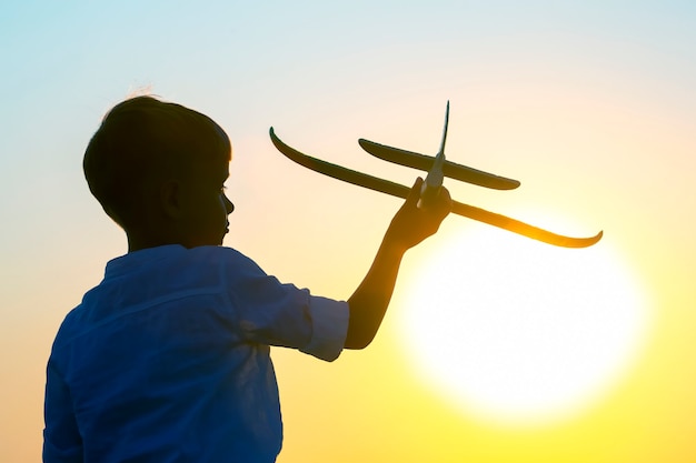 Silhouet van een jongen laat een modelvliegtuig de lucht in vliegen tegen de achtergrond van de ondergaande zon. Kinderdroom van een toekomstige piloot