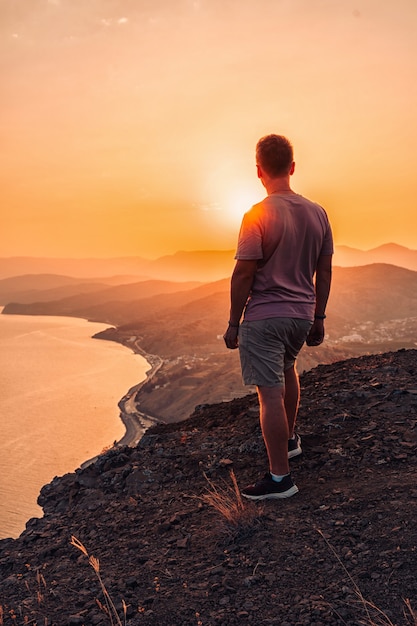 Silhouet van een man bij zonsondergang op een klif met een prachtig landschap en uitzicht op de zee a