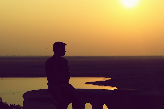 Silhouet van een man die bij de zee zit bij zonsondergang