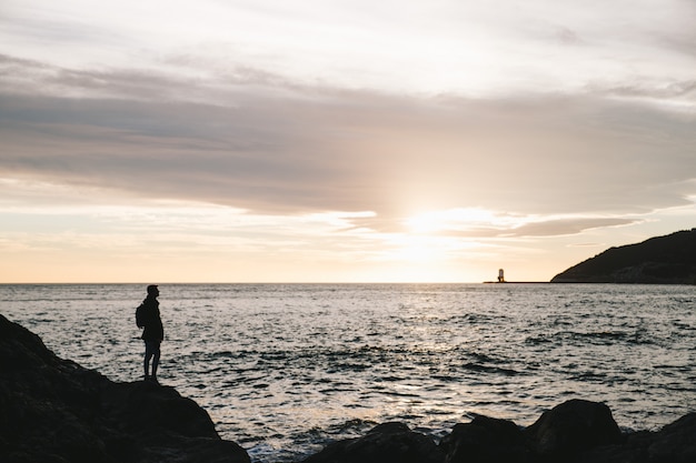 Silhouet van een man die in de rots op een zonsondergang in het strand staat