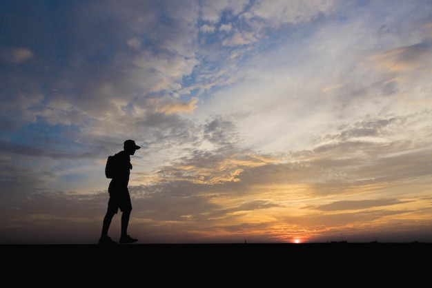 Silhouet van een man gelukkig wandelen bij zonsondergang.