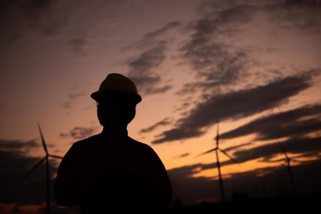 Silhouet van een man-ingenieur die werkt en het rapport vasthoudt bij het Power Generator Station van het windturbinepark op mensen in bergThailand