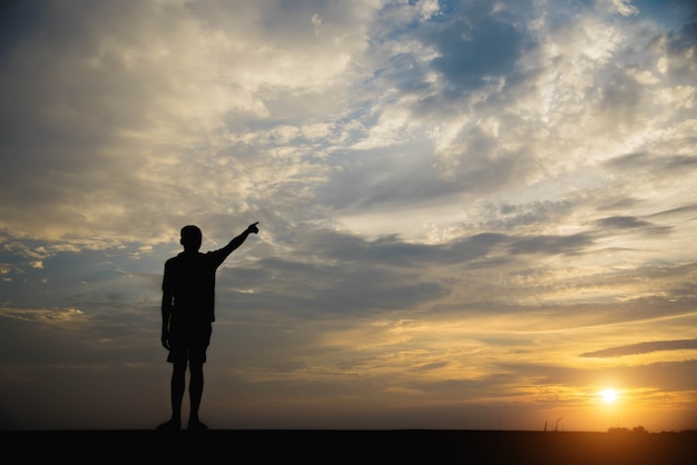 Silhouet van een man met handen wijzen naar de hemel in de zonsondergang.