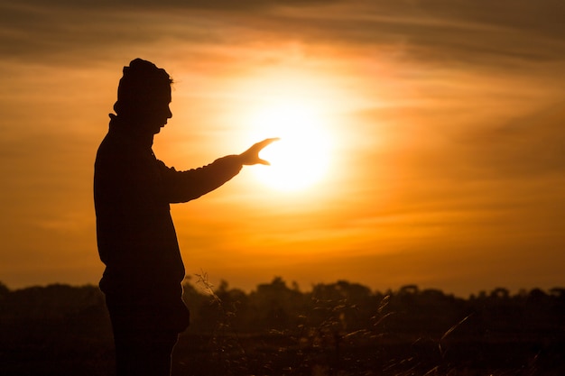 Silhouet van een man permanent en stijgen zijn handen in de lucht tijdens zonsondergang