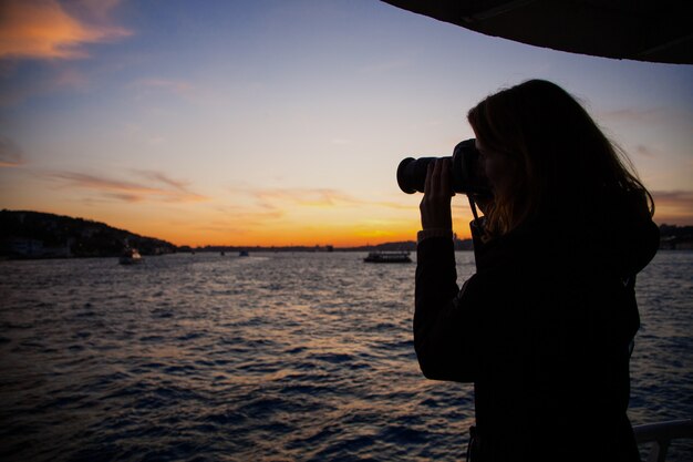 Silhouet van een meisje dat een foto van de boot op het bord van een veerboot bij zonsondergang in Istanbul