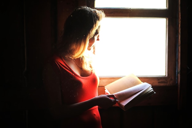 Silhouet van een mooi meisje in een rode jurk op de achtergrond van een raam in een oud huis