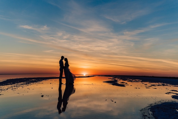 Silhouet van een paar verliefd bij zonsondergang op het strand, weerspiegeld in het water