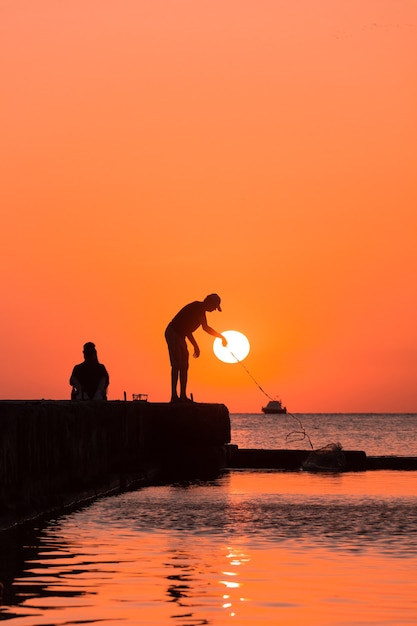 silhouet van een persoon die bij zonsondergang vist