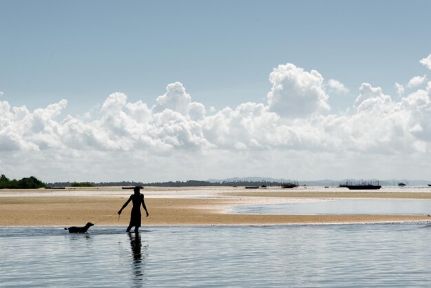 Silhouet van een persoon en een hond lopen langs de rand van het strand van Cabucu in de stad Saubara in Bahia