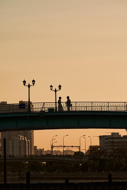 Foto silhouet van een romantisch stel dat's avonds hand in hand op de brug loopt.