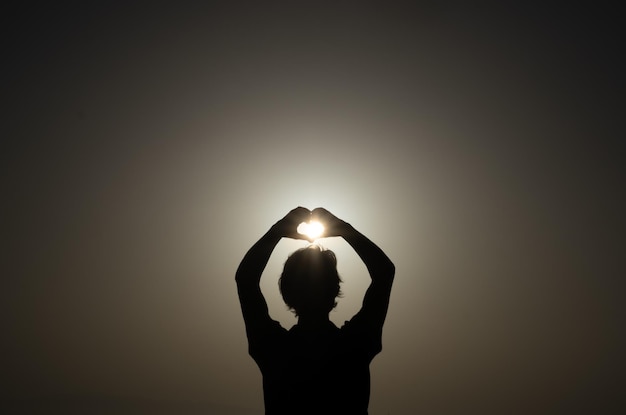 Silhouet van een volwassen blanke vrouw die buiten bij zonsondergang staat en een hartvorm maakt met de handen